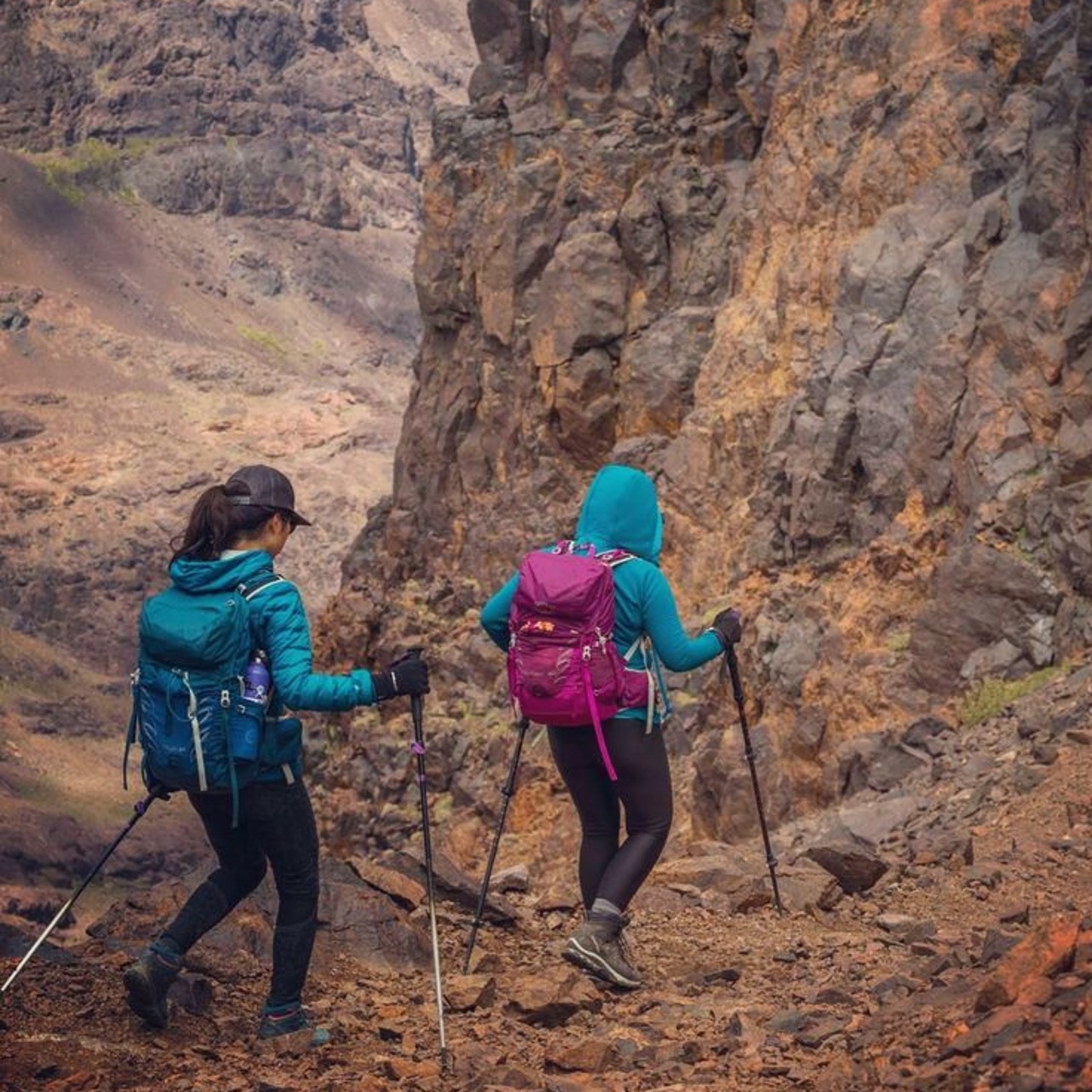 Two trekkers with poles climbing a rocky red-brown trail in the High Atlas